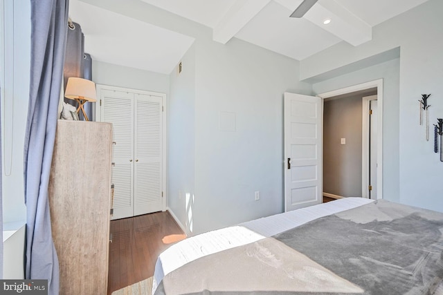 bedroom with beamed ceiling, wood finished floors, a closet, and baseboards