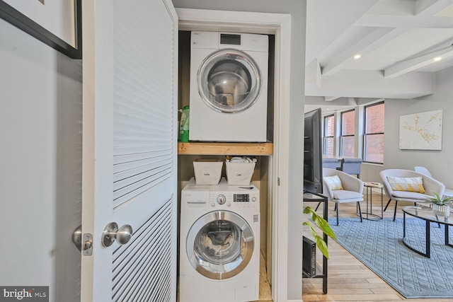 clothes washing area with wood finished floors, laundry area, and stacked washer / dryer