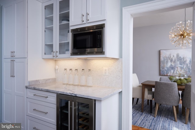 kitchen with light stone counters, wine cooler, white cabinetry, stainless steel microwave, and glass insert cabinets