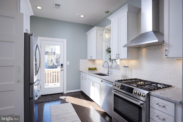 kitchen featuring light stone counters, stainless steel appliances, white cabinetry, a sink, and wall chimney range hood