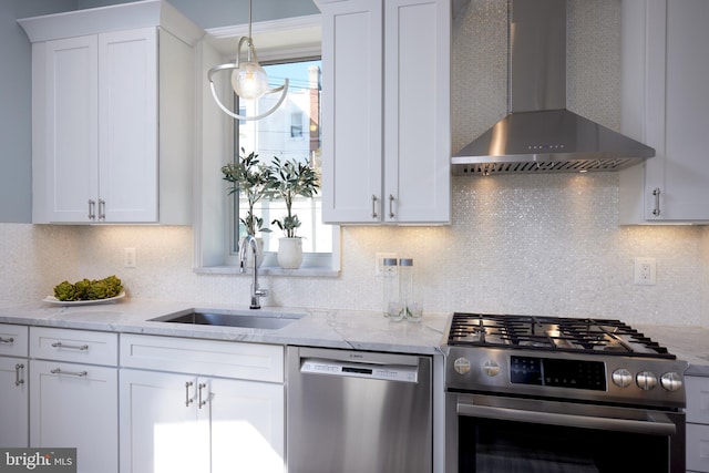 kitchen featuring appliances with stainless steel finishes, white cabinetry, a sink, wall chimney range hood, and light stone countertops