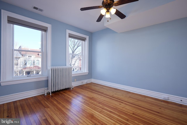 empty room with radiator, baseboards, visible vents, and hardwood / wood-style floors