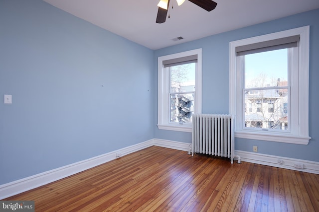 empty room featuring dark wood-style flooring, baseboards, visible vents, and radiator heating unit