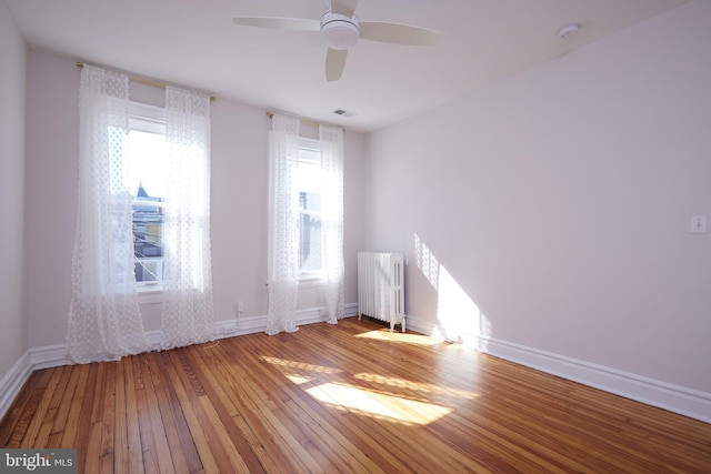 empty room with baseboards, ceiling fan, hardwood / wood-style floors, and radiator heating unit