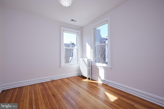 unfurnished room featuring visible vents, baseboards, light wood finished floors, and radiator heating unit