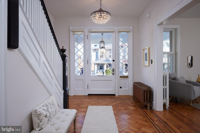 foyer featuring an inviting chandelier, radiator heating unit, and stairway