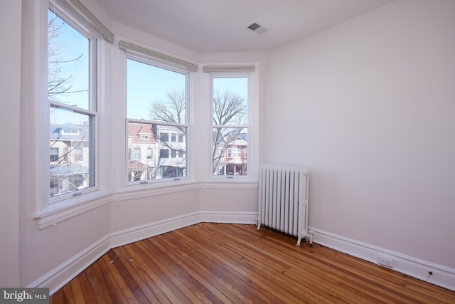 empty room featuring baseboards, visible vents, radiator heating unit, and hardwood / wood-style flooring