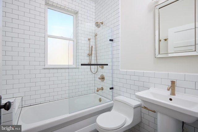 full bath featuring tile walls, shower / bathing tub combination, toilet, wainscoting, and a sink