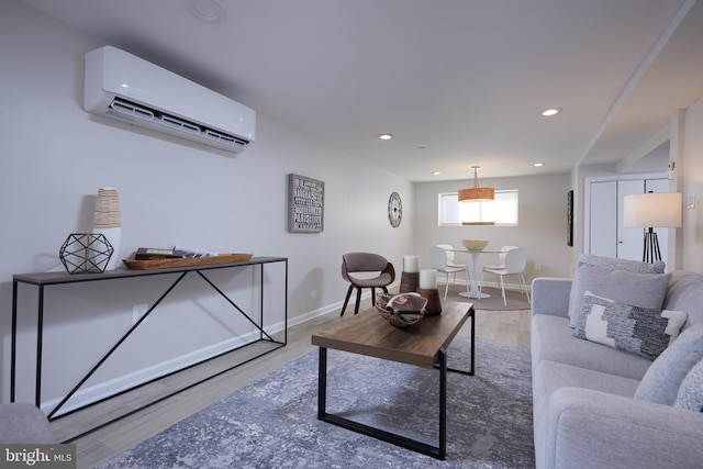 living room featuring a wall unit AC, light wood-style floors, baseboards, and recessed lighting