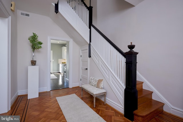 staircase featuring a towering ceiling, visible vents, and baseboards