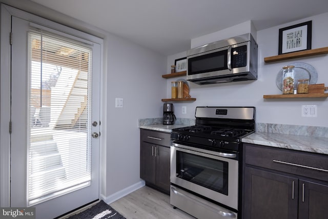 kitchen featuring dark brown cabinetry, light wood-style flooring, appliances with stainless steel finishes, light countertops, and open shelves