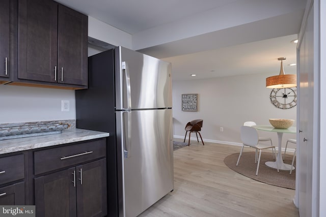 kitchen featuring light wood-style flooring, baseboards, dark brown cabinets, freestanding refrigerator, and decorative light fixtures