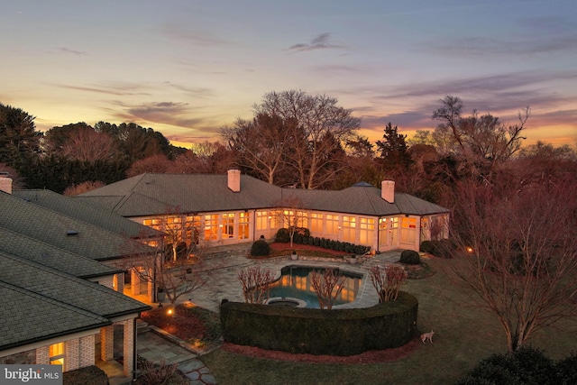 back of house at dusk featuring a patio area, a chimney, and an outdoor pool