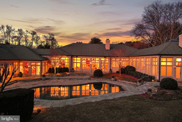 pool at dusk with a patio area and an outdoor pool