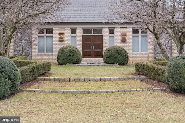 property entrance featuring brick siding, a shingled roof, and a yard