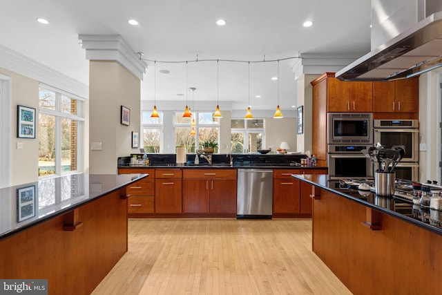 kitchen featuring range hood, appliances with stainless steel finishes, brown cabinetry, and decorative light fixtures