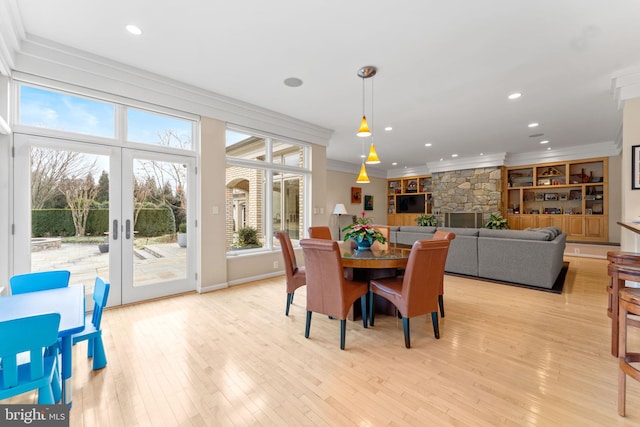 dining room with light wood-style floors, a stone fireplace, crown molding, and french doors