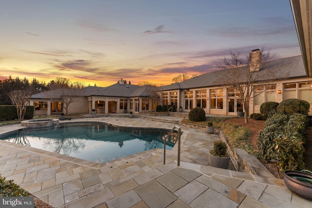 pool at dusk with a patio area and a pool with connected hot tub