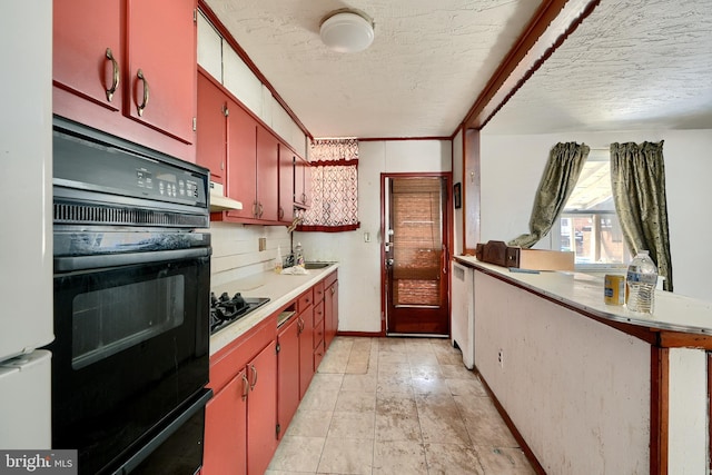 kitchen with a textured ceiling, under cabinet range hood, light countertops, red cabinets, and black appliances