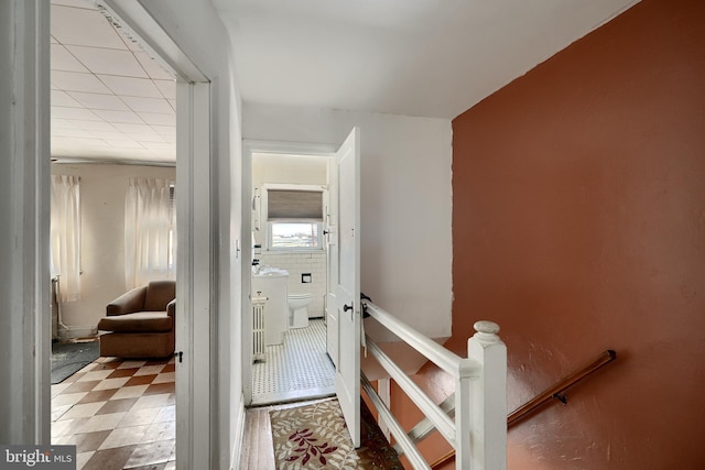 hall with tile walls and an upstairs landing