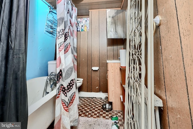 bathroom with toilet, wood walls, and tile patterned floors