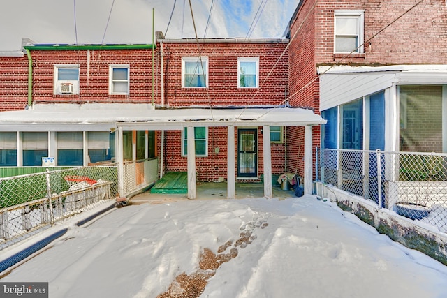 snow covered rear of property featuring brick siding and fence