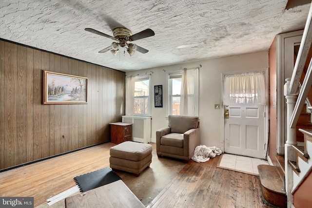 unfurnished room with a ceiling fan, radiator heating unit, a textured ceiling, light wood-type flooring, and wood walls