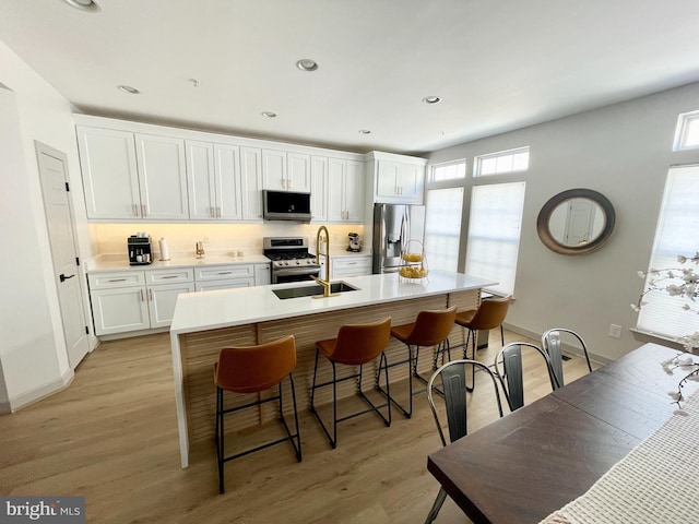 kitchen featuring appliances with stainless steel finishes, white cabinetry, light wood-type flooring, and a sink