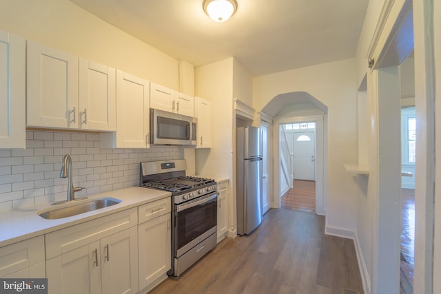 kitchen with stainless steel appliances, a sink, white cabinetry, light countertops, and backsplash