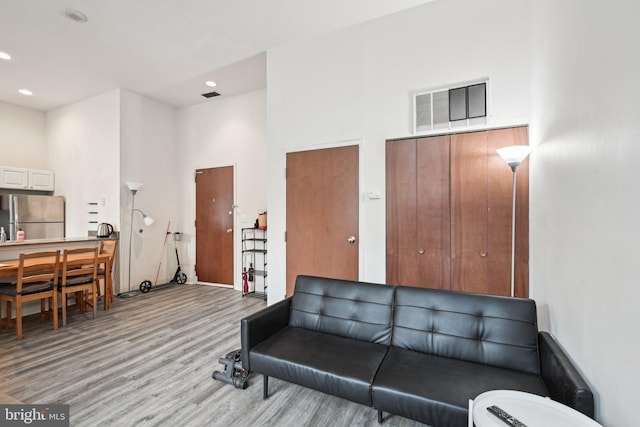 living area featuring recessed lighting, visible vents, a towering ceiling, and light wood finished floors