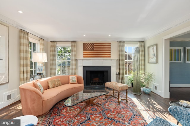 living area featuring wood finished floors, visible vents, baseboards, a fireplace with flush hearth, and ornamental molding