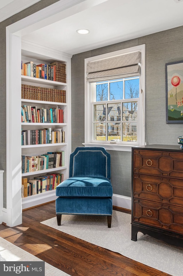 living area featuring wallpapered walls, built in shelves, wood finished floors, and baseboards