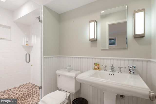 bathroom with a sink, a shower stall, toilet, and wainscoting