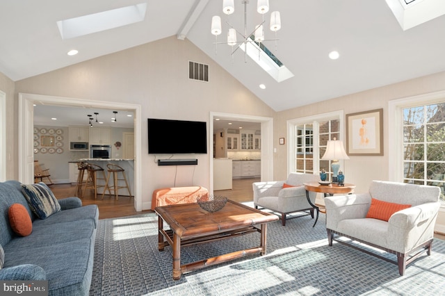 living area with visible vents, a skylight, wood finished floors, a notable chandelier, and high vaulted ceiling