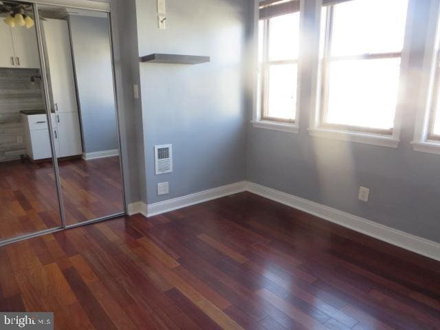 unfurnished bedroom with baseboards, visible vents, dark wood finished floors, and a closet