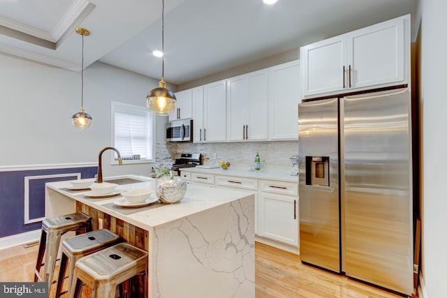 kitchen with light stone counters, pendant lighting, stainless steel appliances, white cabinetry, and an island with sink