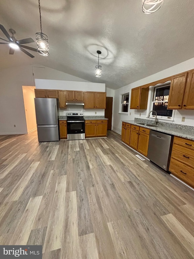 kitchen with stainless steel appliances, light wood-style floors, brown cabinetry, and a sink