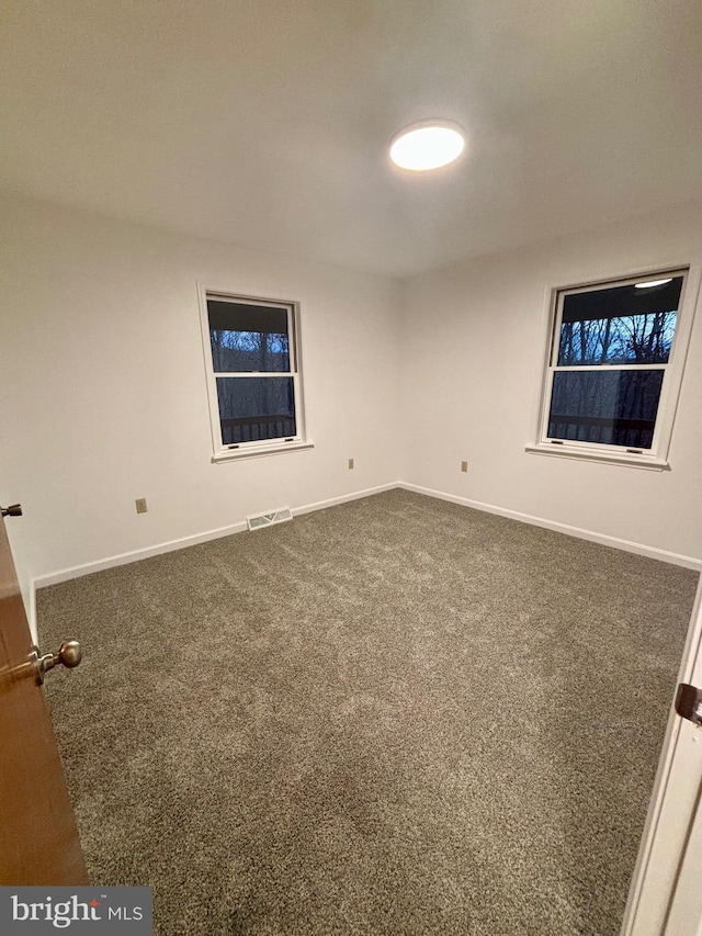 unfurnished room with dark colored carpet, visible vents, and baseboards