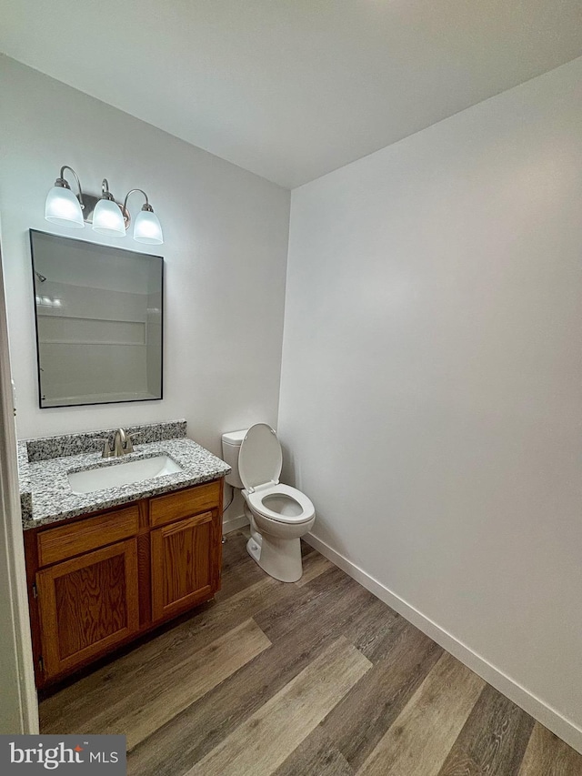 bathroom featuring toilet, baseboards, wood finished floors, and vanity