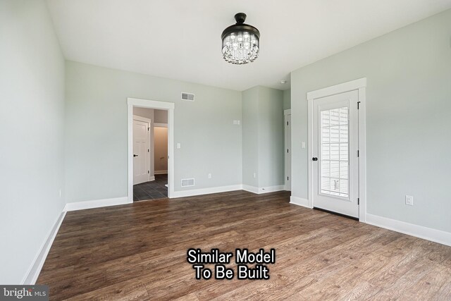 spare room with visible vents, dark wood finished floors, a notable chandelier, and baseboards