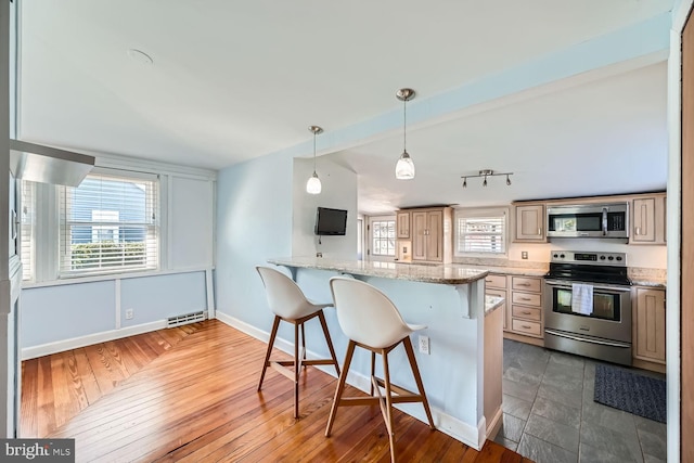 kitchen featuring appliances with stainless steel finishes, a kitchen breakfast bar, a peninsula, light stone countertops, and pendant lighting