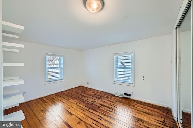 unfurnished bedroom featuring a closet, multiple windows, wood finished floors, and baseboards