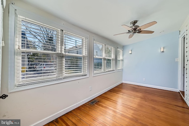 empty room featuring a ceiling fan, visible vents, baseboards, and wood finished floors