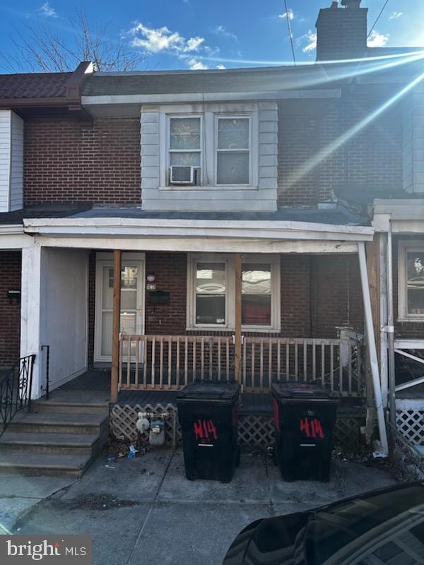 view of property featuring covered porch, a chimney, cooling unit, and brick siding