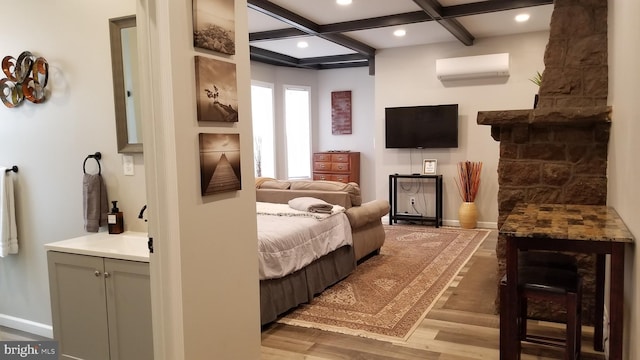 bedroom featuring baseboards, coffered ceiling, wood finished floors, an AC wall unit, and a sink