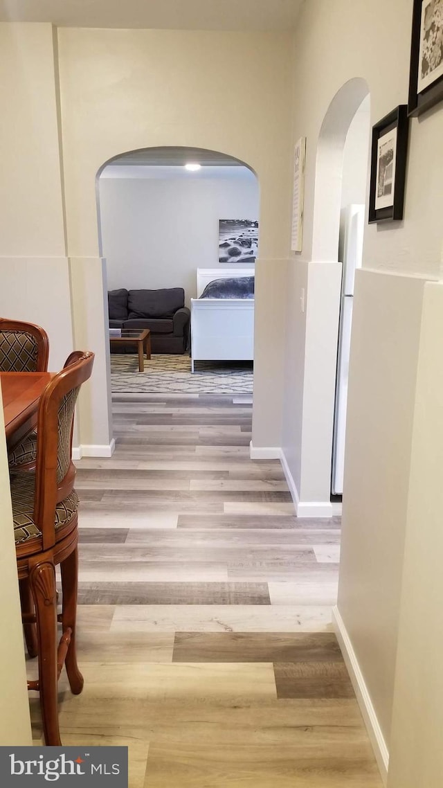 hallway with baseboards, arched walkways, and wood finished floors