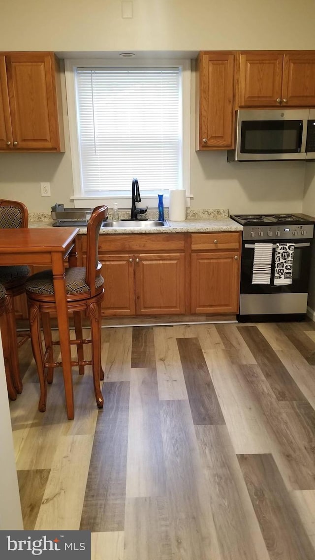 kitchen with stainless steel appliances, brown cabinetry, and light wood finished floors