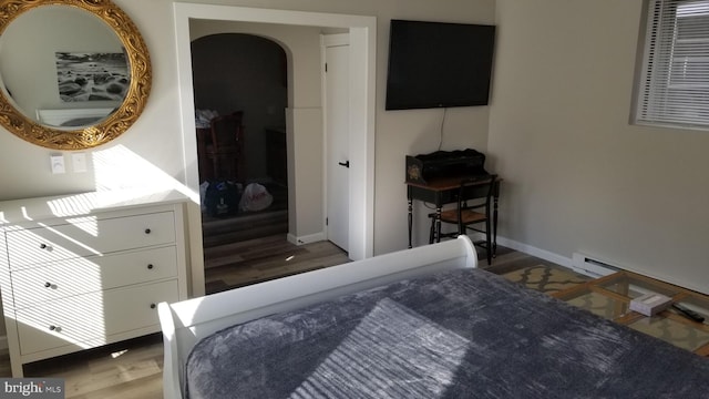 bedroom with baseboards, arched walkways, baseboard heating, and wood finished floors