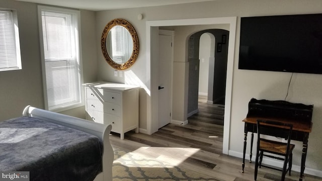 bedroom with arched walkways, light wood-style flooring, and baseboards