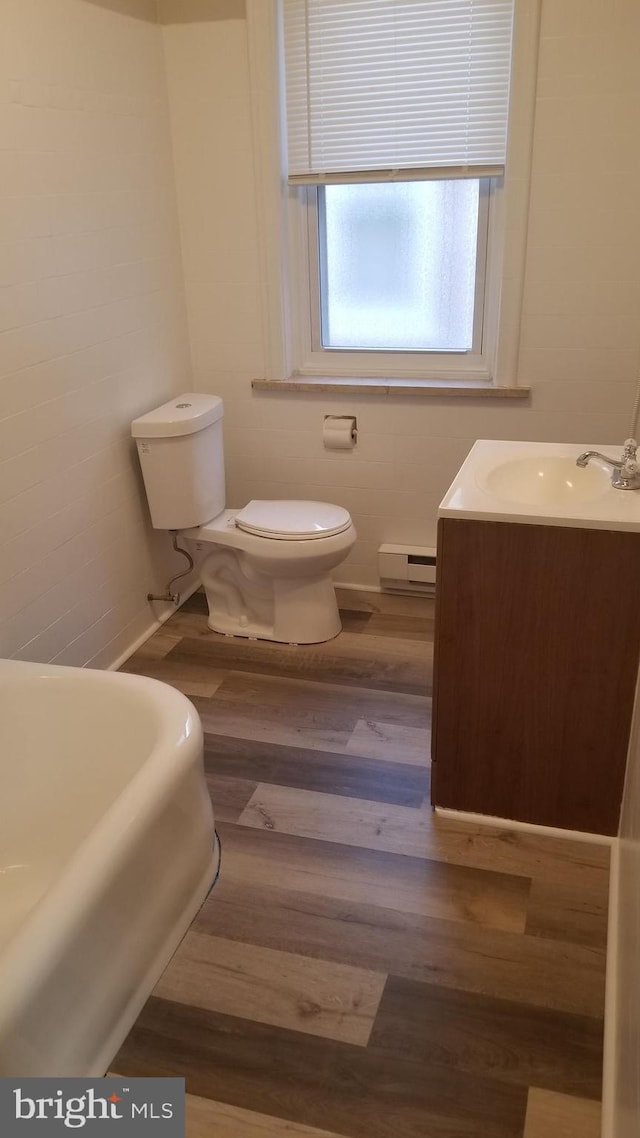 full bathroom with toilet, a washtub, wood finished floors, vanity, and baseboard heating